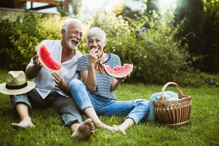 senior couple having fun while eating watermelon in the backyard