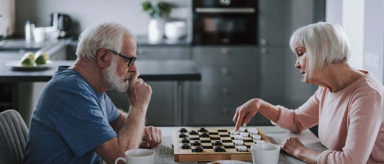 Elderly pensioner couple playing checkers at home
