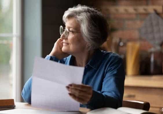 thoughtful_senior_woman_holding_paper_document_smiling_into_the_distance