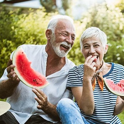 senior-couple-having-fun-while-eating-watermelon-in-the-backyard-1000x429