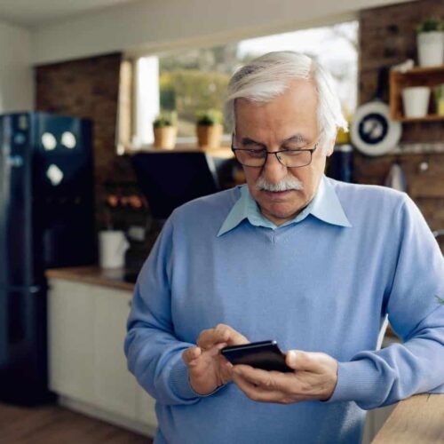 Senior man text messaging on mobile phone in the kitchen